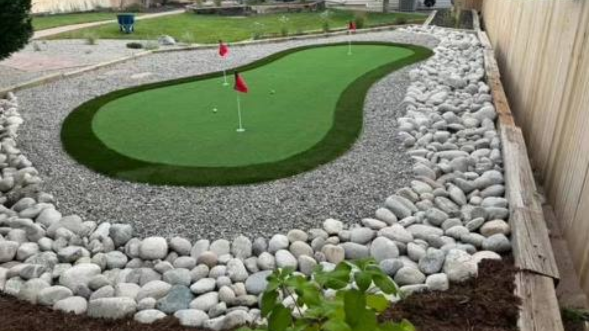 Backyard putting green surrounded by decorative rock and river rock border.