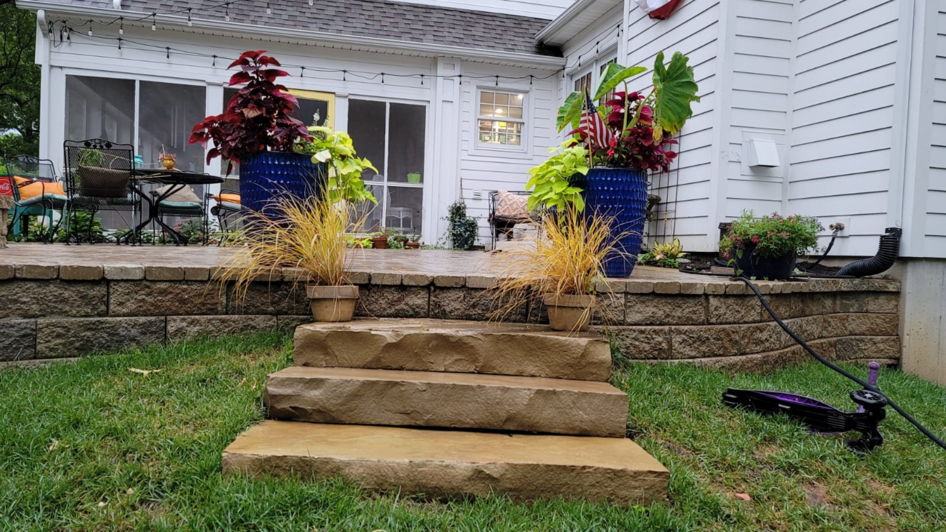 Backyard stone steps leading to raised patio with planters and paver surface.