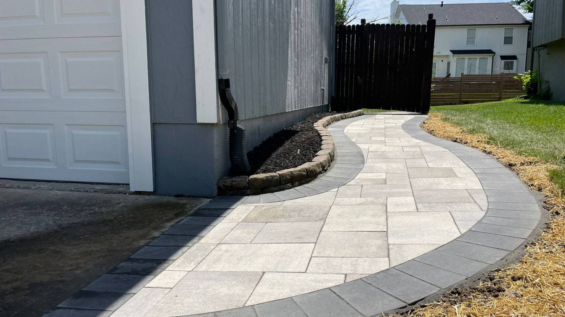 Curved side yard paver walkway with dark border and fresh landscape bed.