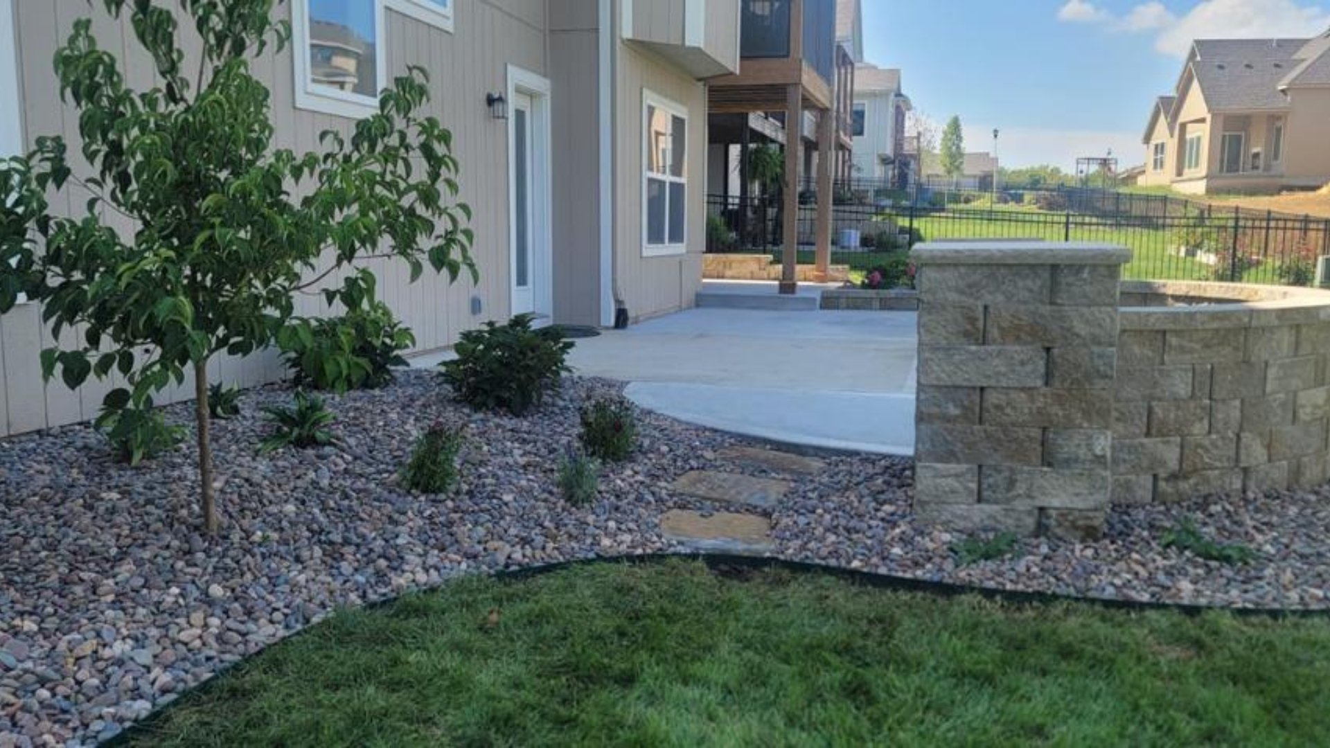 Curved stone wall with decorative rock bed and new landscape plantings.