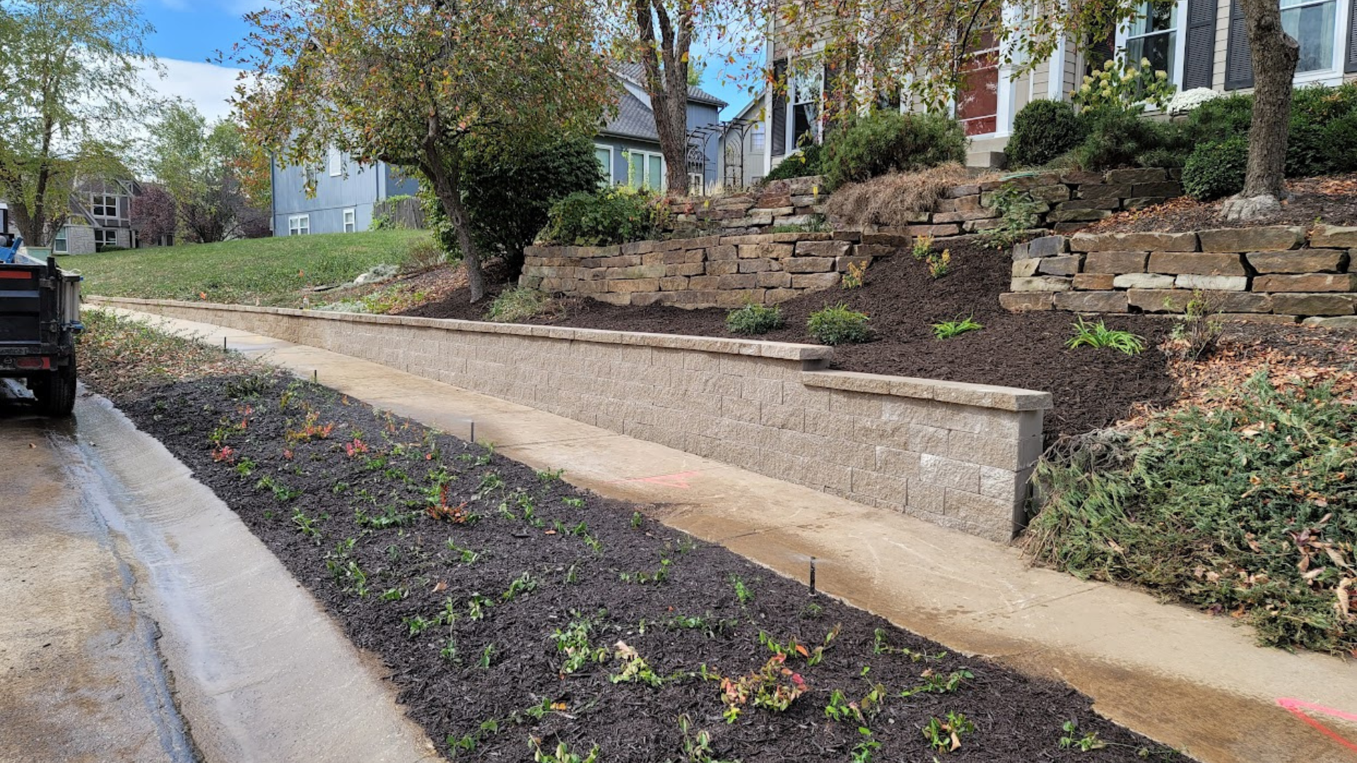 Large retaining wall with sidewalk, mulch bed, and hillside landscaping.