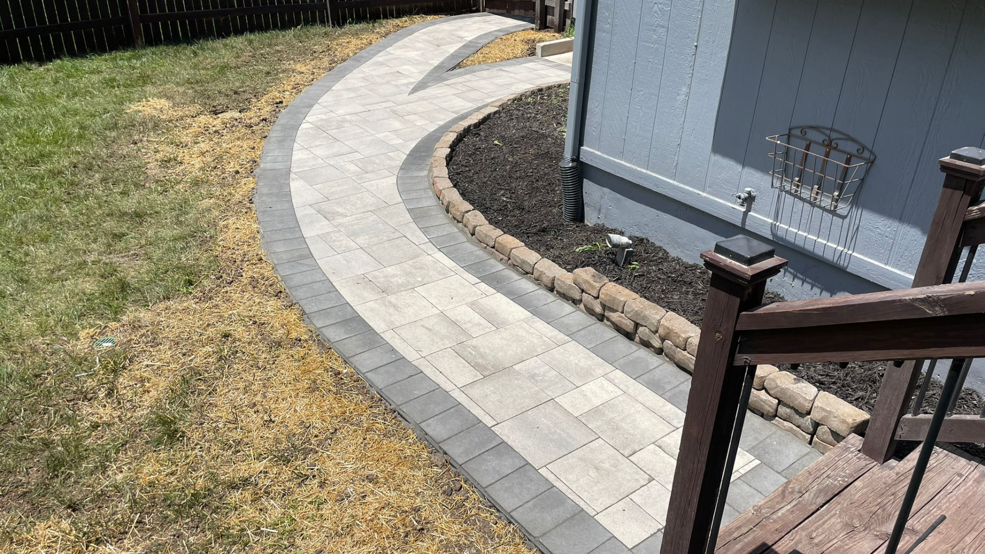 Modern curved paver walkway with dark border and mulched foundation bed.
