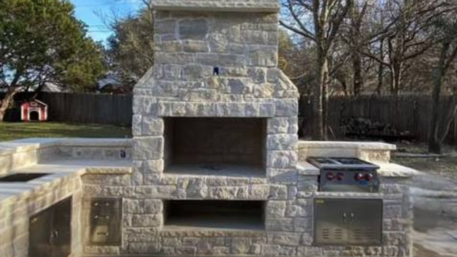 Outdoor stone fireplace with built-in grill, storage, countertops, and seating walls.