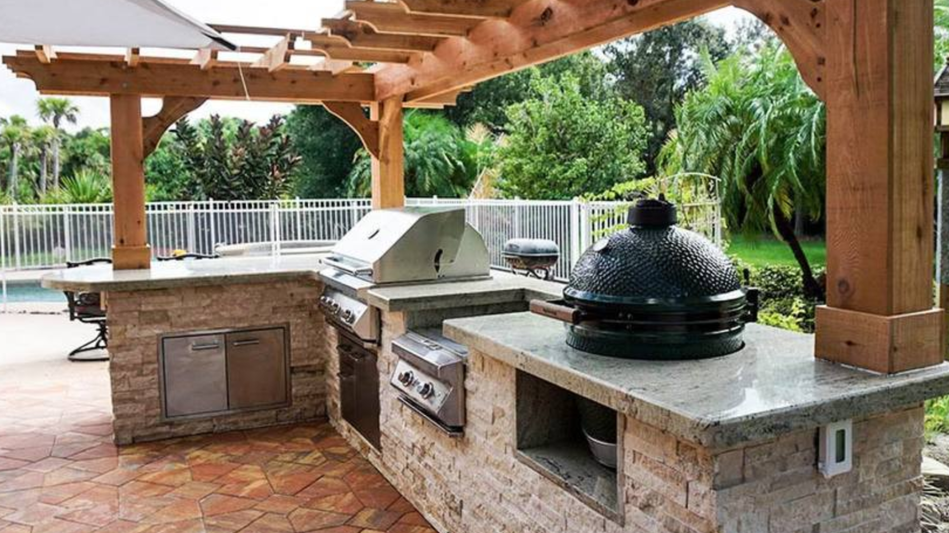Outdoor kitchen with stone bar, built-in grill, pergola, and patio area.