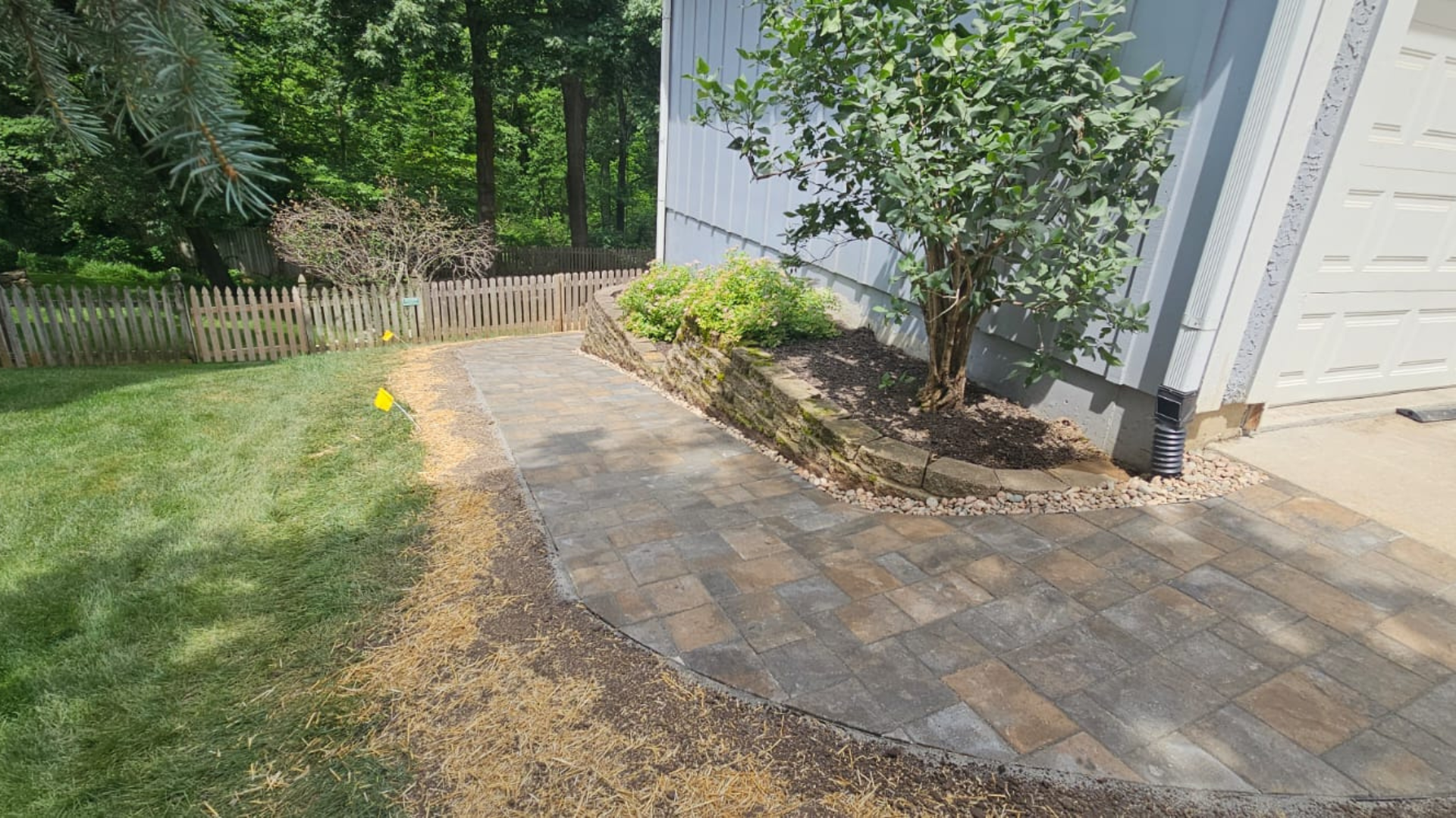 Paver walkway with retaining wall, mulch bed, shrubs, and side yard landscaping.