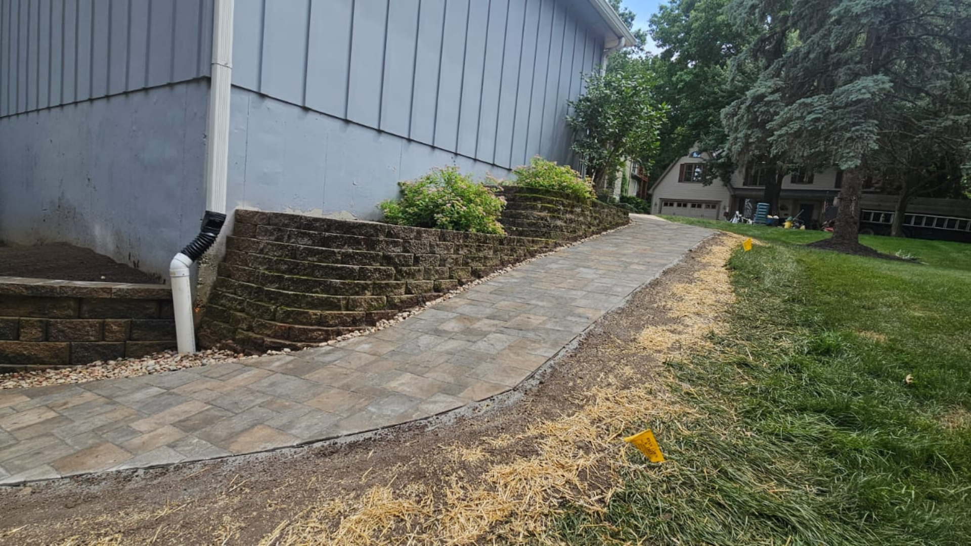 Side yard paver walkway installed along a retaining wall and sloped lawn.