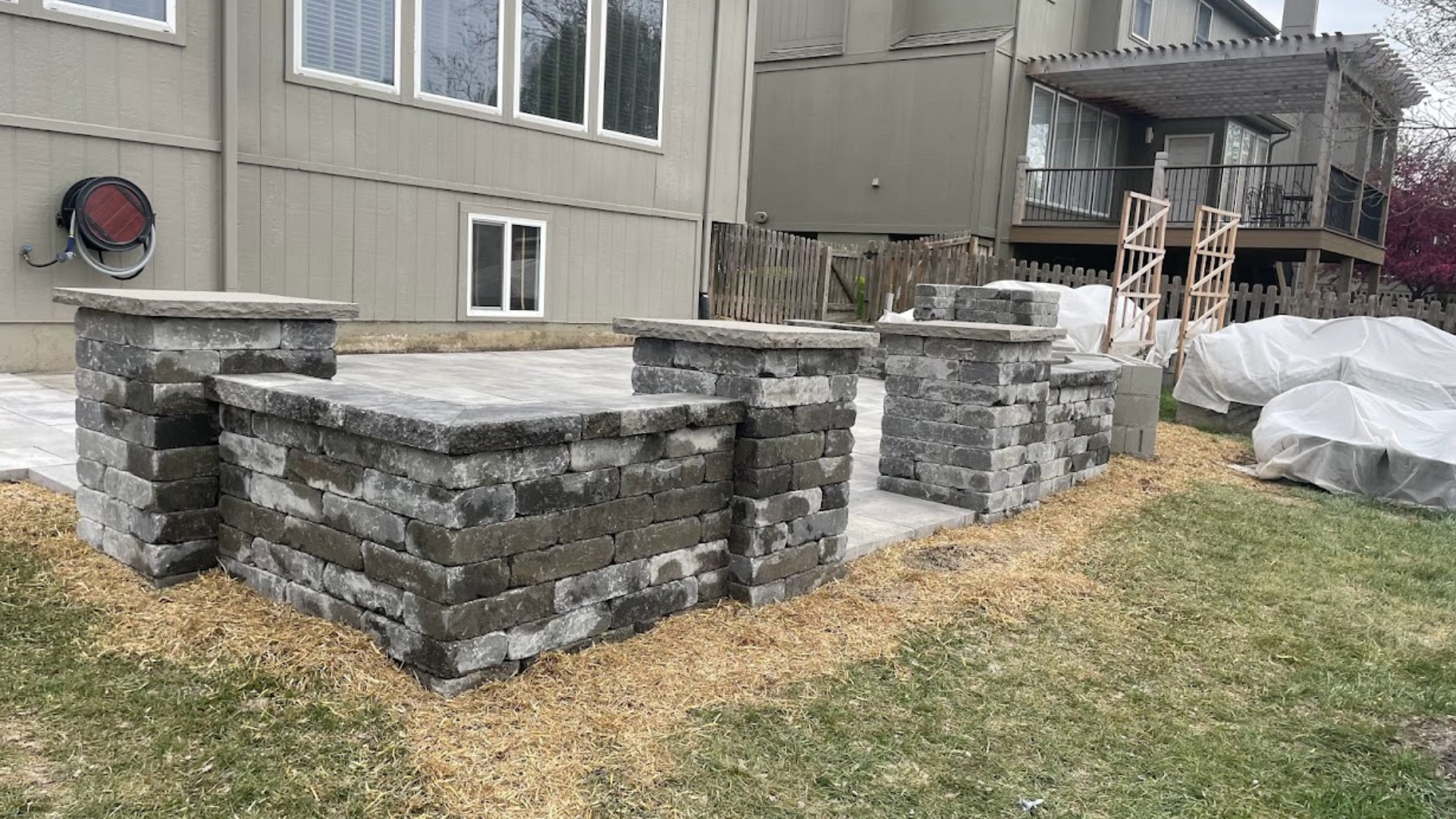Raised paver patio with stone pillars, steps, and retaining wall structure.