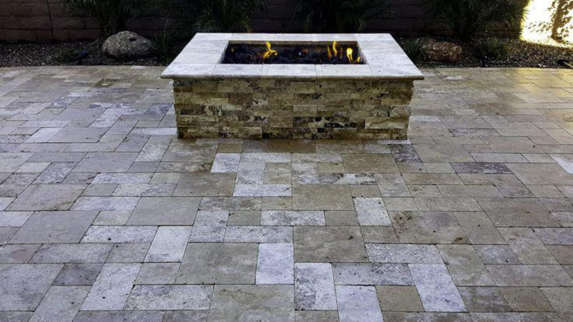 Rectangular gas fire pit on paver patio with stone surround and landscape wall.