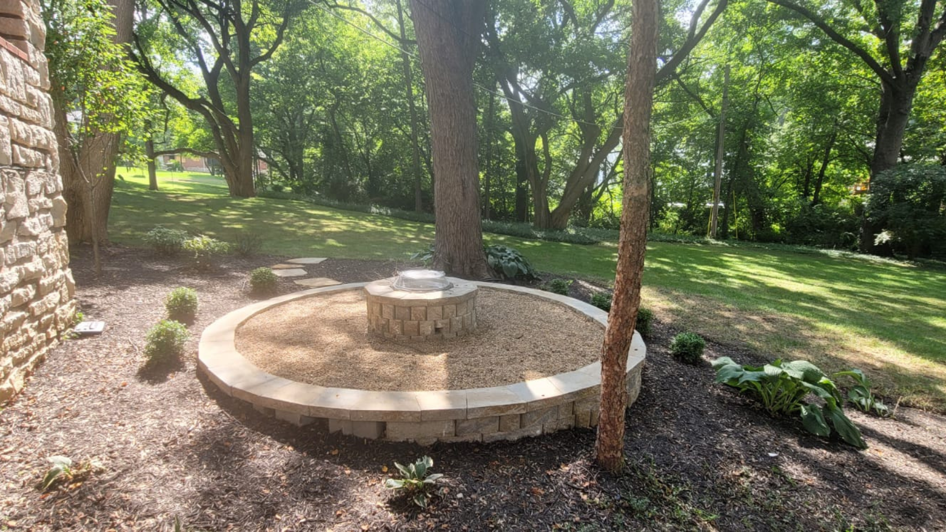 Round stone fire pit with outdoor chairs, gravel border, and backyard seating area.