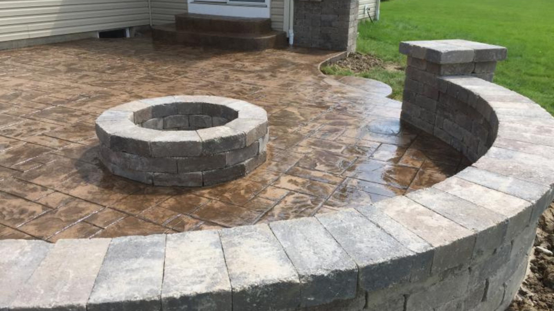 Stamped concrete patio with circular fire pit and curved stone seating wall.
