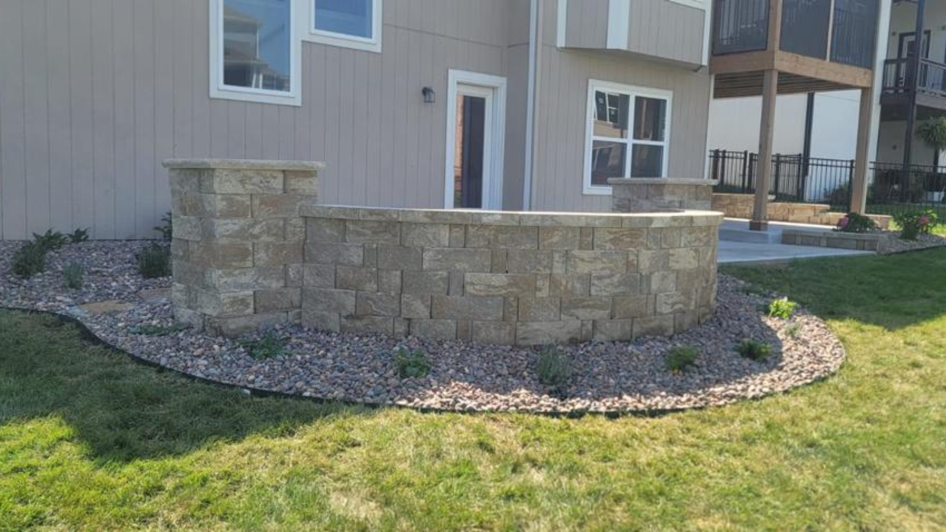 Curved stone seating wall with decorative rock landscape and lawn area.