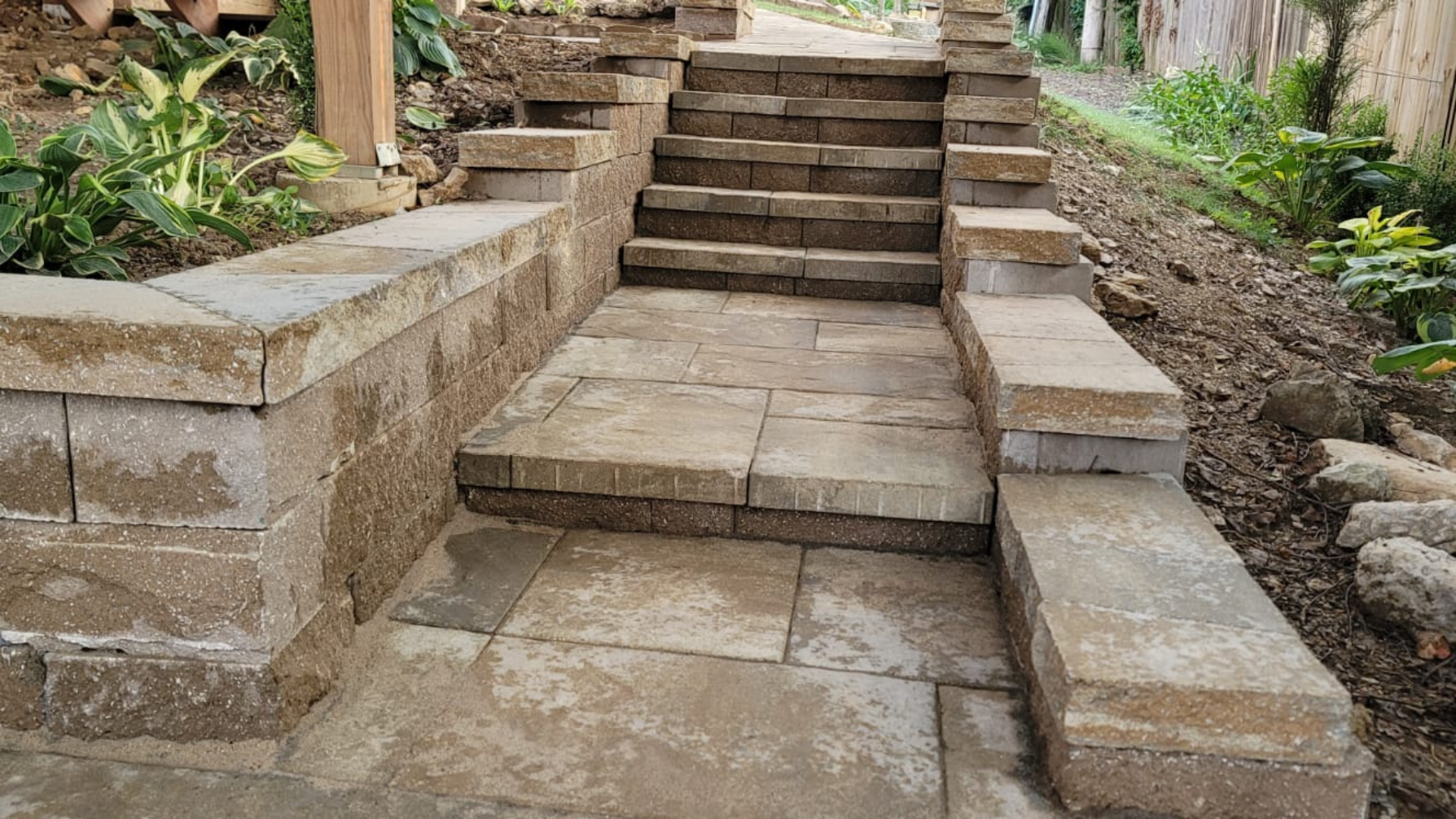 Stone steps with retaining walls and paver landing in a landscaped backyard.