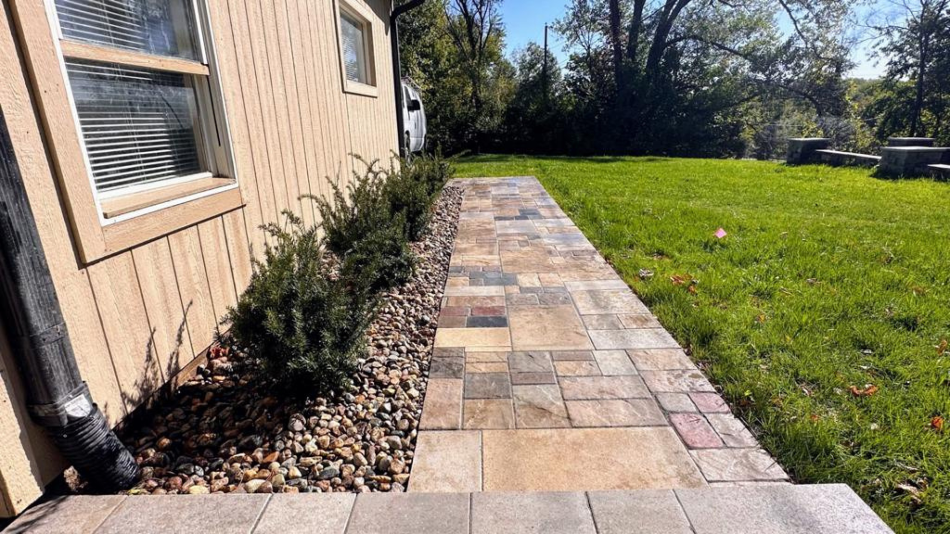 Straight paver walkway with decorative rock bed and shrubs along the house.