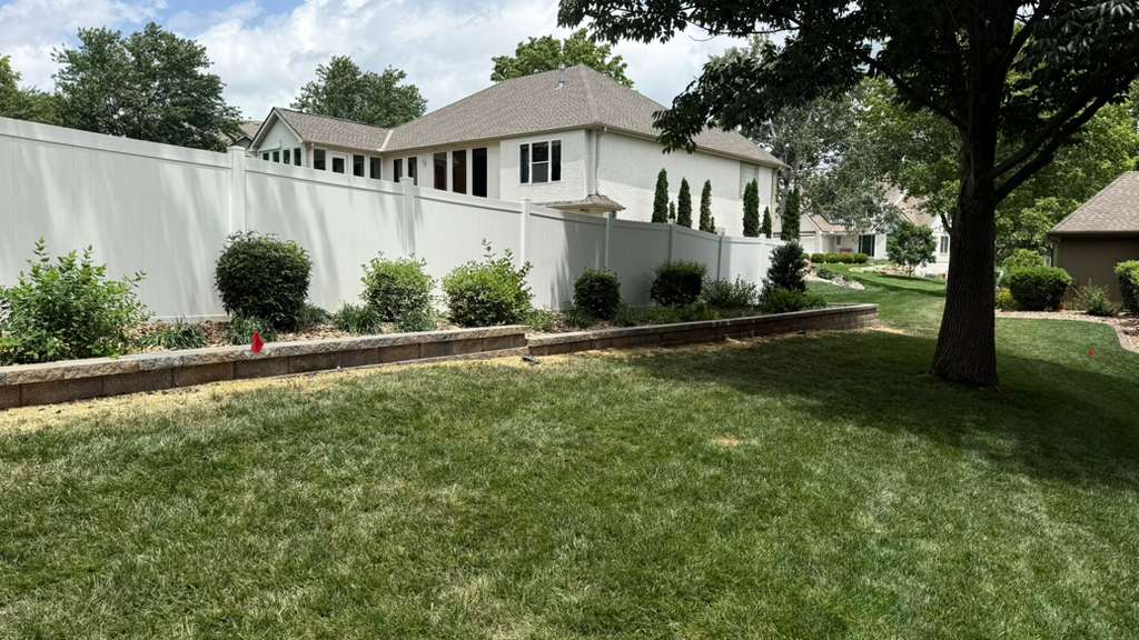 Fence Line Landscape Bed and Lawn Care in Leawood Kansas Well-maintained backyard lawn with fence line landscape bed, evergreen shrubs, decorative rock, and clean grass in Leawood Kansas