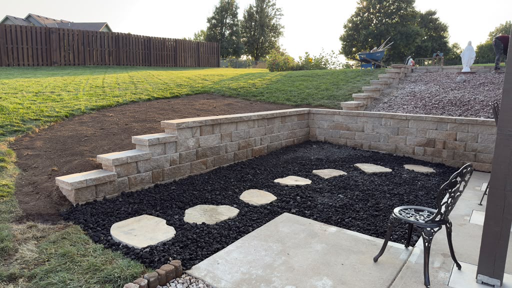 Retaining wall with built-in steps, black decorative rock, and natural stone stepping path in a landscaped backyard
