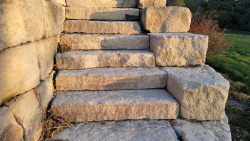Natural stone steps create a strong and timeless transition through the landscape. Natural stone steps built into a retaining wall with large stone blocks.