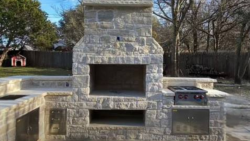 A stone fireplace and outdoor kitchen create a complete backyard entertainment area. Outdoor stone fireplace with built-in grill, storage, countertops, and seating walls.