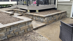 A retaining wall and stair system designed to connect outdoor living areas. Stone retaining wall with steps, patio landing, and raised deck area.