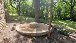 A round stone fire pit creates a cozy backyard seating area. Round stone fire pit with outdoor chairs, gravel border, and backyard seating area.