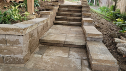 Stone steps and retaining walls create a strong, finished backyard entrance. Stone steps with retaining walls and paver landing in a landscaped backyard.