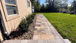 A clean paver walkway paired with low-maintenance decorative rock. Straight paver walkway with decorative rock bed and shrubs along the house.